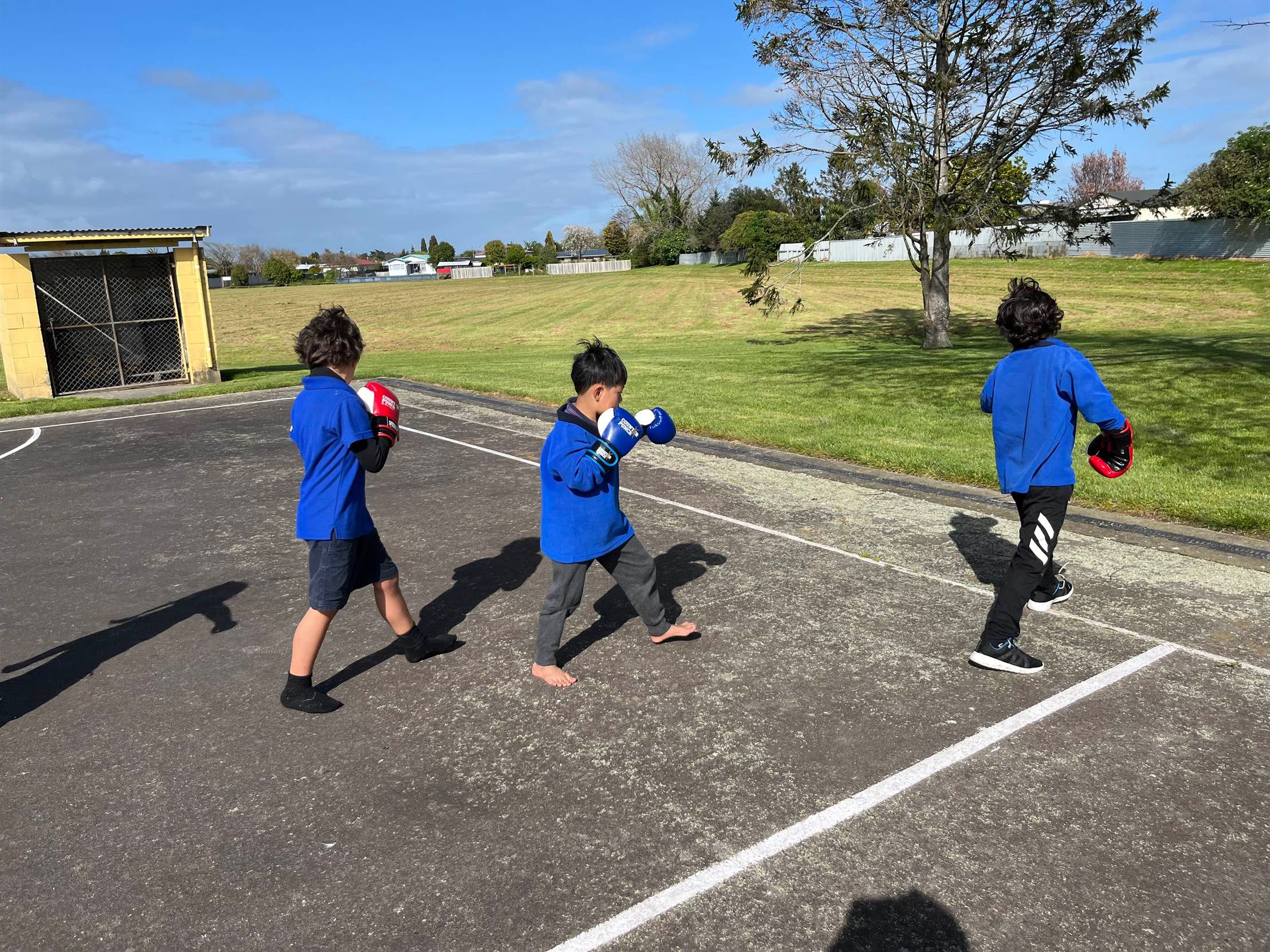 Tamariki boxing outdoors on a school court.