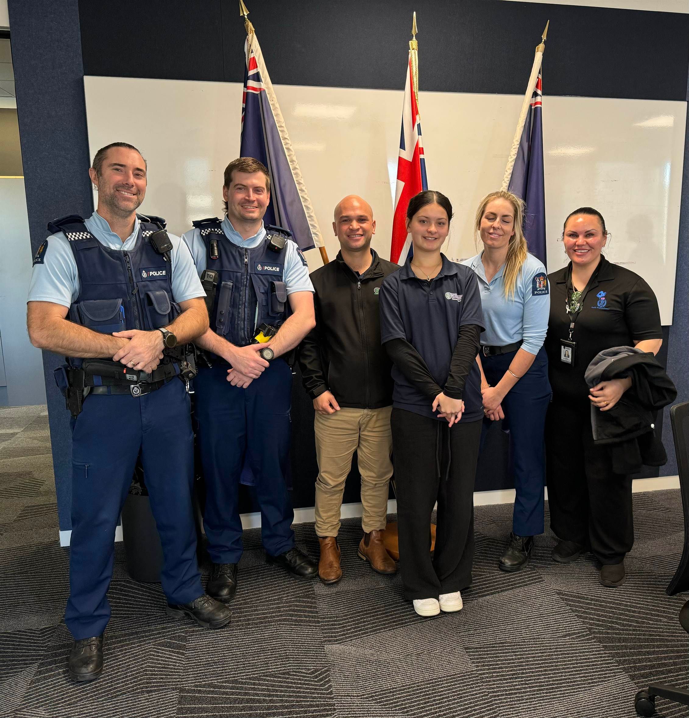 Josh Te Rauna with New Zealand Police staff in front of the New Zealand and Police flags.